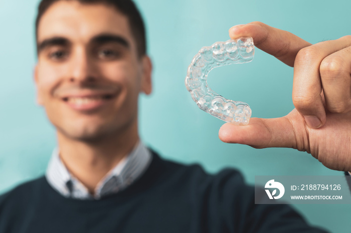 A man posing with orthodontic resin splints. Alteration of invisible teeth. The mobile orthodontic appliance for dental correction comes out in the foreground, concept of bruxism.