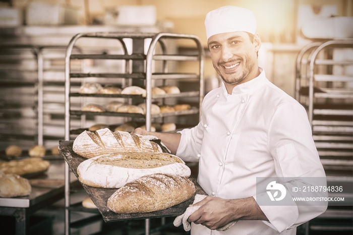 Smiling baker holding tray of bread