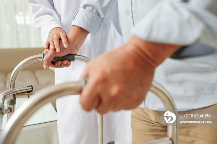 Close-up of female nurse helping to get up the man with walker at retirement home