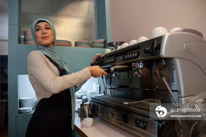 Young woman in hijab making coffee in cafe