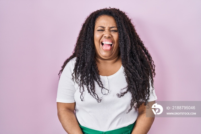 Plus size hispanic woman standing over pink background sticking tongue out happy with funny expression. emotion concept.