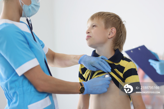 Female pediatrician listening to boy kid breathing with stethoscope tool, appointment at doctor