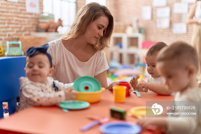 Teacher and preschool students learning to eat sitting on table at kindergarten