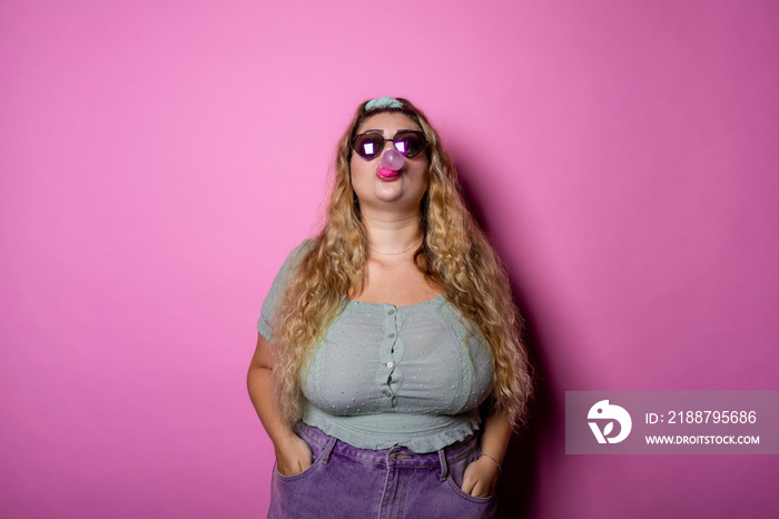 Young woman blowing bubble gum while standing indoors