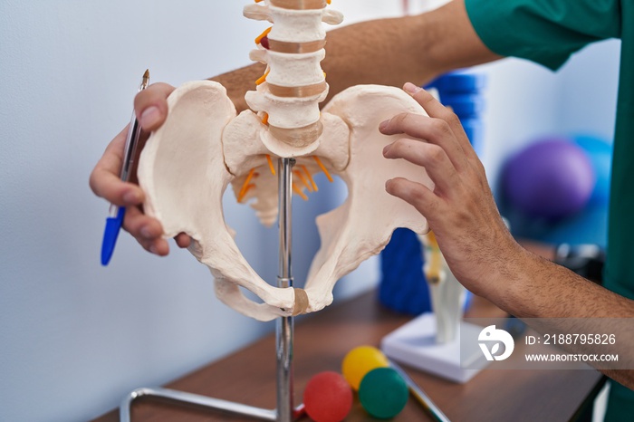 Young caucasian man physiotherapist touching anatomical model of spinal column at rehab clinic