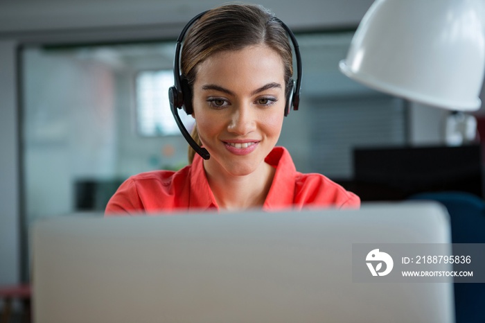 Smiling female executive working on her laptop while calling