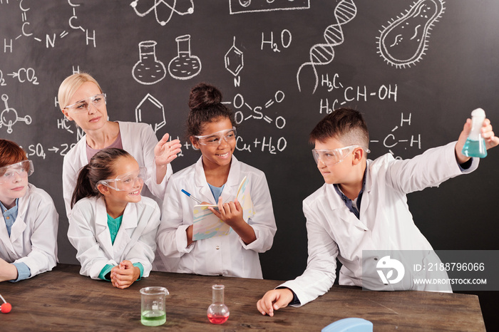 Blond teacher and intercultural schoolkids looking at chemical reaction in tube