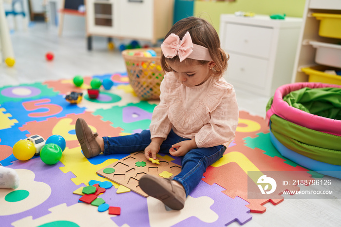 Adorable blonde toddler playing with maths puzzle game sitting on floor at kindergarten