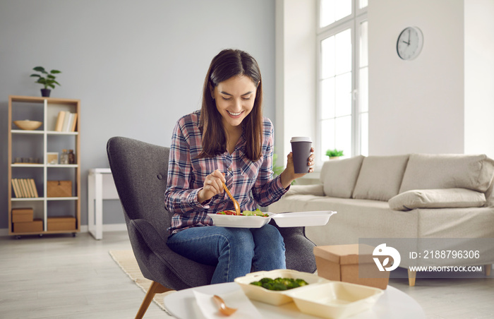 Woman eating delicious takeout lunch at home. Happy lady sitting in armchair in living room, drinking coffee, holding food container on lap, and enjoying tasty veggie salad from from takeaway delivery