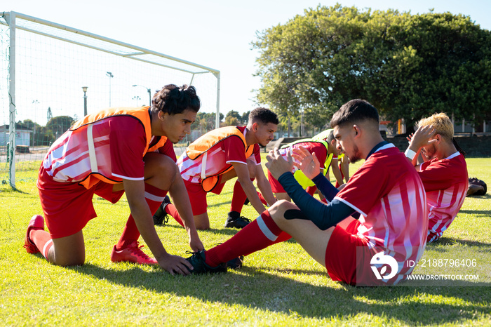 Male players holding legs of multiracial teammates practicing crunches on grassy field at playground