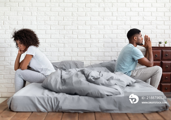 Couple sitting back to back on bed during conflict