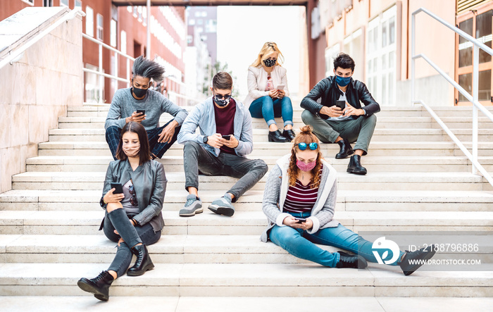 Urban milenial people using mobile phones covered by face mask on Covid third wave - Worried guys and girls watching video on smartphone - University students sitting at study break - Bright filter