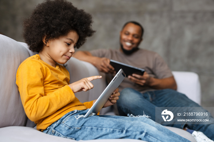 Black father and son using tablet computers while sitting on sofa