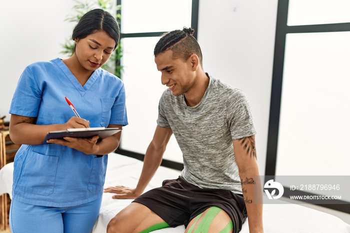 Young latin physioterapist woman asking to patient at the clinic.