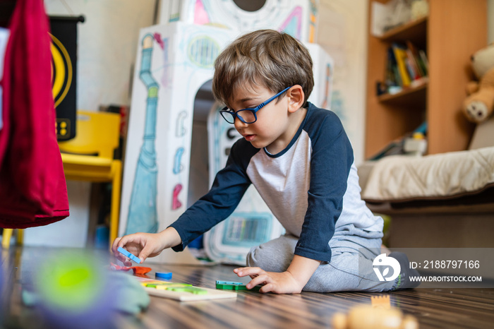 Portrait of happy caucasian boy with eyeglasses sitting at home in room in day real people small male playful child playing on the floor