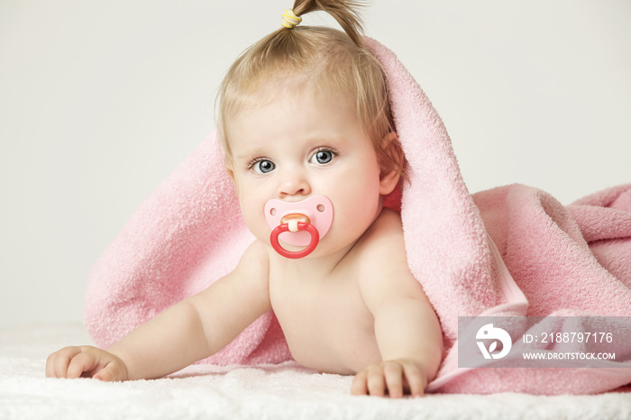 Studio portrait of adorable baby girl with pacifier covered with towel