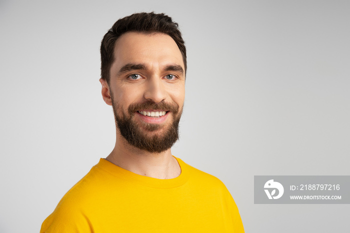 portrait of joyful bearded man in yellow t-shirt looking at camera isolated on grey.