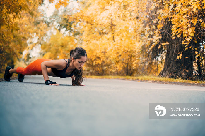 Fit woman doing push ups in autumn park.