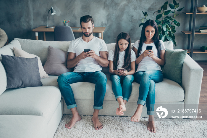 Portrait of nice attractive lovely concentrated focused family wearing casual white t-shirts jeans denim sitting on sofa using 5g browsing at industrial style interior living-room