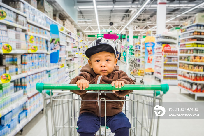 Asian baby boy sitting on the trolley while shopping aisle in the supermarket. Little kid on the shopping cart while buying groceries in the store. Concept of breastfeeding early childhood development