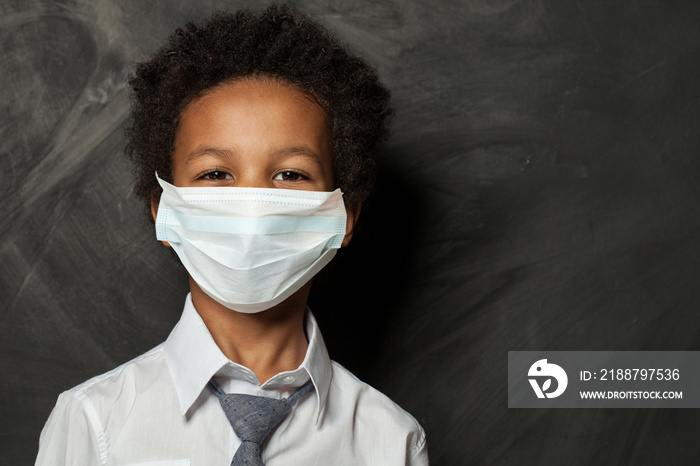 Black child boy in medical protective face mask on blackboard background