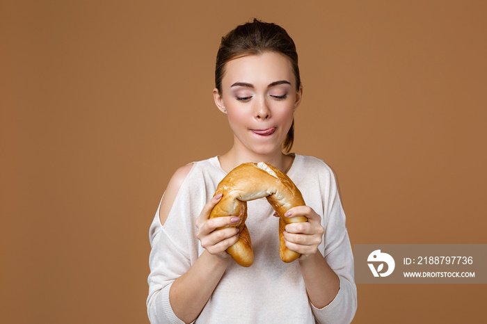 Portrait of beautiful young woman eating delicious bread baguette on studio yellow background. girl with fresh fragrant long loaf