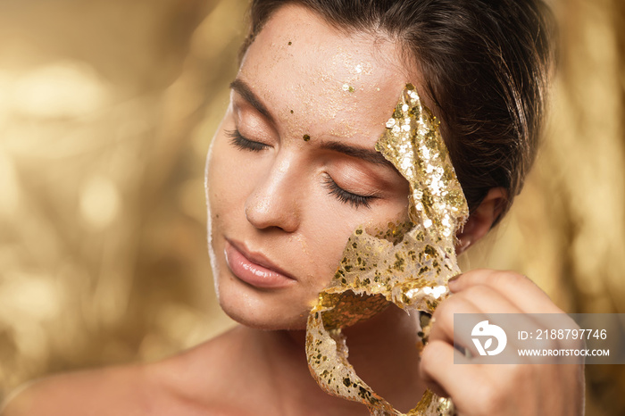 Beautiful woman with golden shining mask on her face for skin treatment