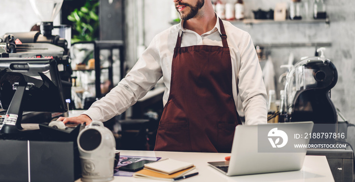 Portrait of handsome bearded barista man small business owner working with laptop computer behind the counter bar in a cafe