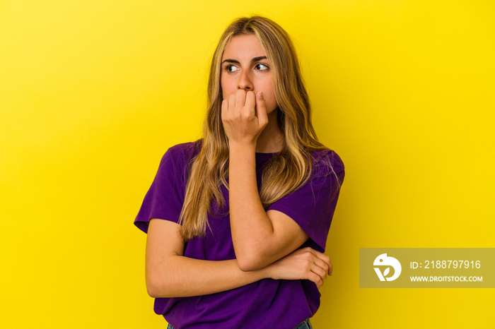 Young blonde caucasian woman isolated on yellow background biting fingernails, nervous and very anxious.