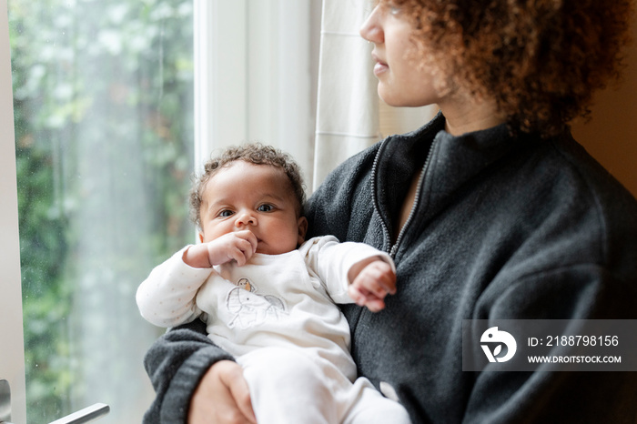 Mother holding baby daughter and looking out window