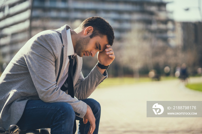 Young businessman is sitting in park after being fired. He is depressed.