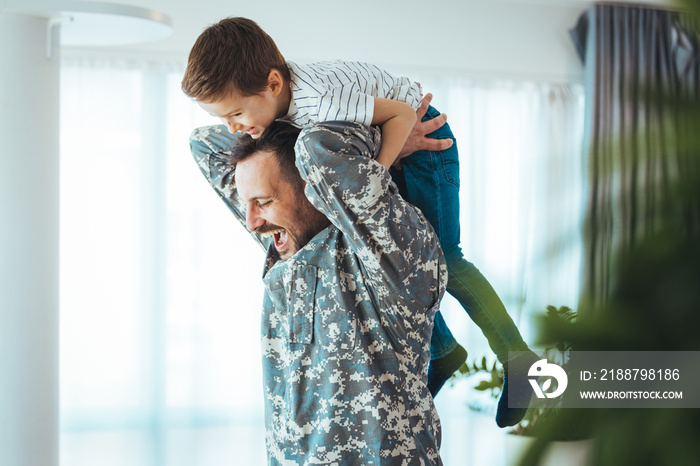 Soldier and his little son hugging at home. Smiling soldier reunited with his son after coming back from war. Military soldier father with son kid smiling during home return - Family love US army