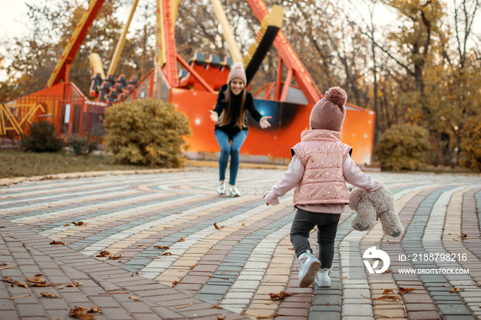 Young female woman babysitter and toddler baby girl walk in autumn park. Happy family mom and toddler outdoors in fall park.