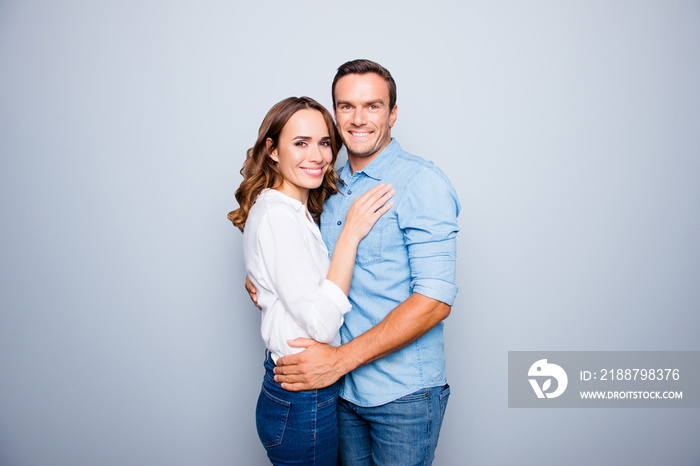 He vs she happy together. Close up portrait of cute, adult couple in casual outfit hugging, looking at camera standing over grey background