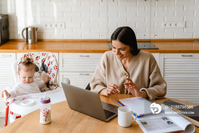 Young mother working with laptop while keeping her baby at home