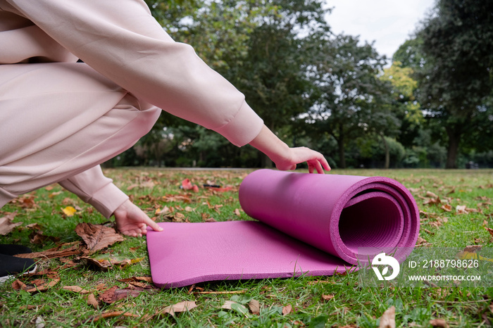 Close-up of woman unrolling yoga mat on grass in park