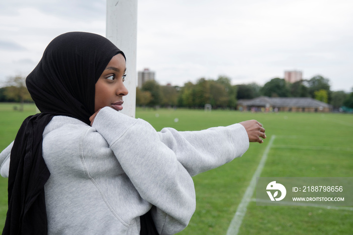 Portrait of woman in hijab stretching arm in soccer field