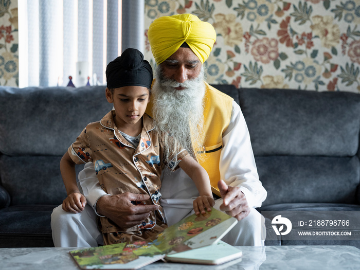 Grandfather and grandson (6-7) in traditional clothing reading book