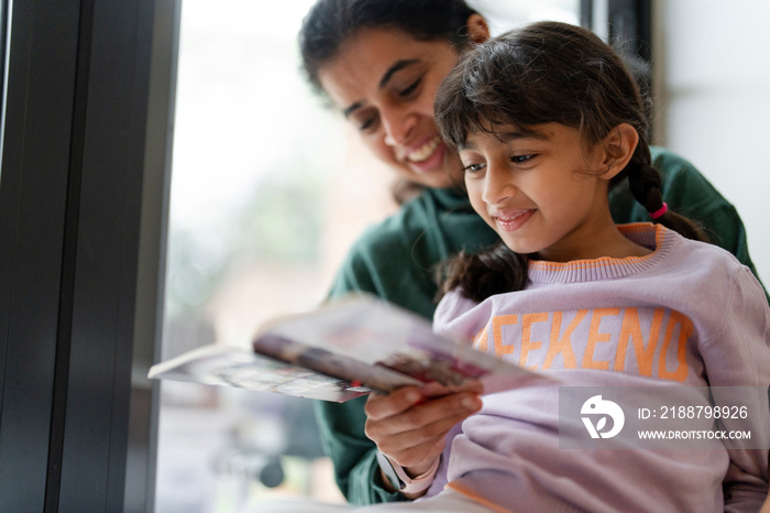 Mother and daughter reading book near window