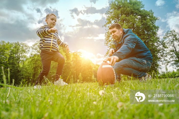 Father and son playing football, Father’s day, Playful Man teaching Boy rugby outdoors in sunny day at public park. Family sports weekend.