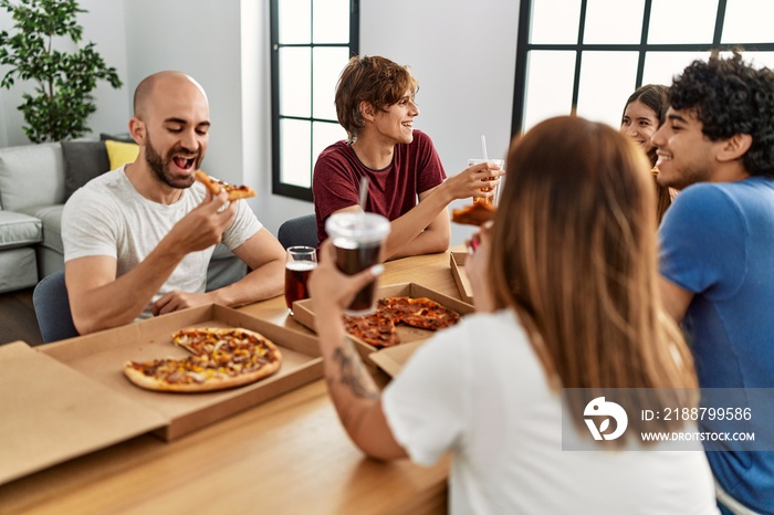 Group of young friends smiling happy eating italian pizza sitting on the table at home.