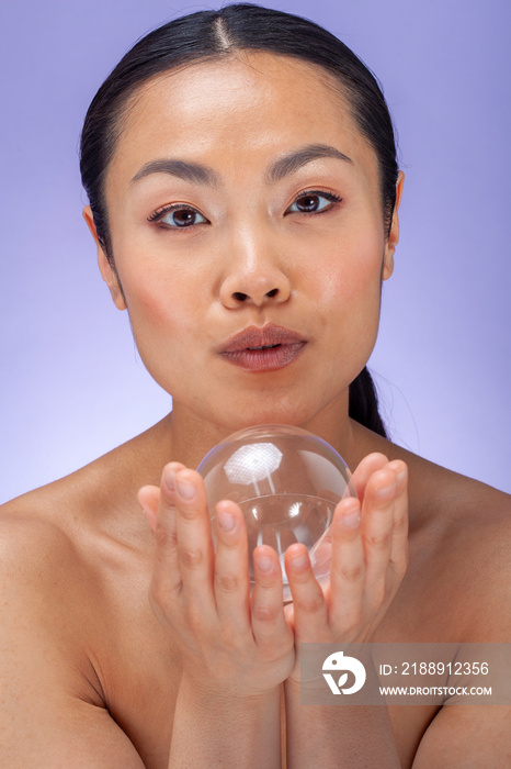 Studio portrait�of woman holding soap bubble against purple background