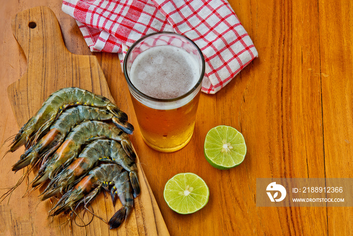 Fresh prawns, lime and glass of beer on a wooden background. Kitchen Background.