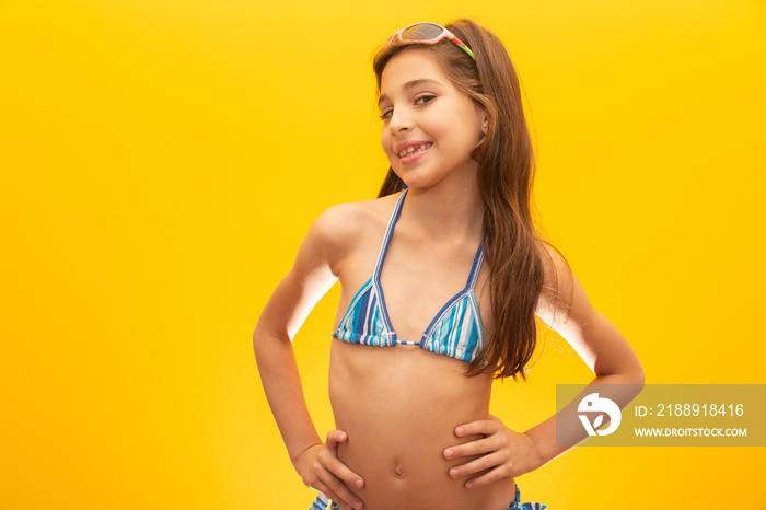 Child wearing bikini on yellow background. Concept of summer, beach and pool.