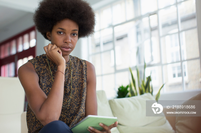 Portrait young woman with afro using digital tablet on sofa