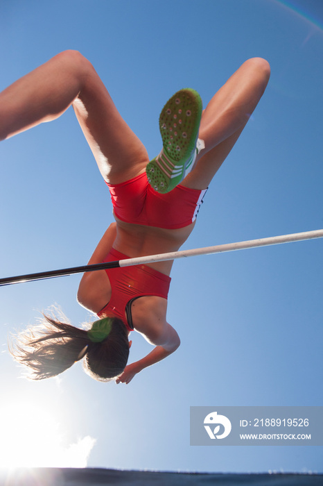 Female track and field athlete high jumping under sunny sky