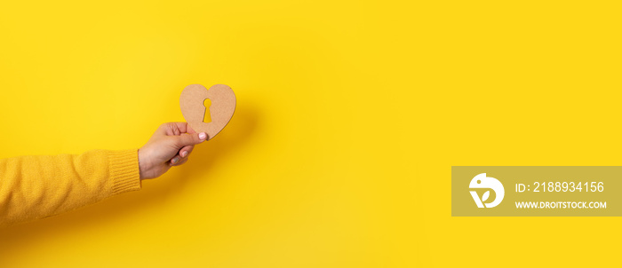 wooden heart with keyhole in hand over yellow background