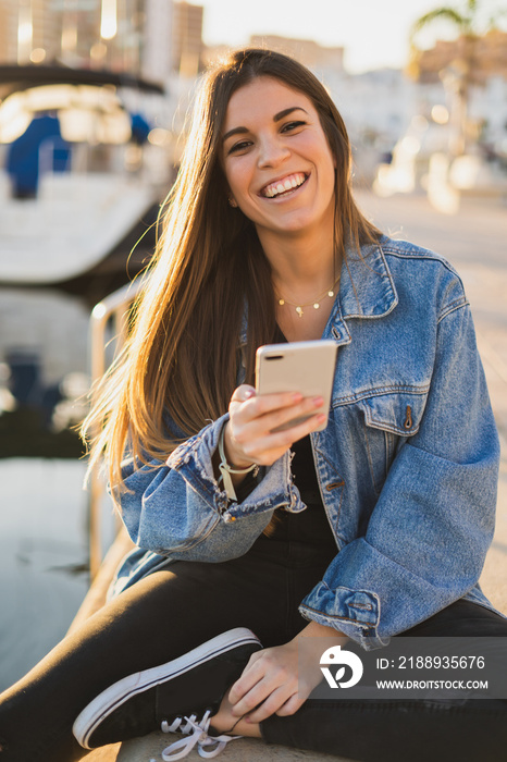 Happy woman smiling and sitting in the sea port using a smartphone