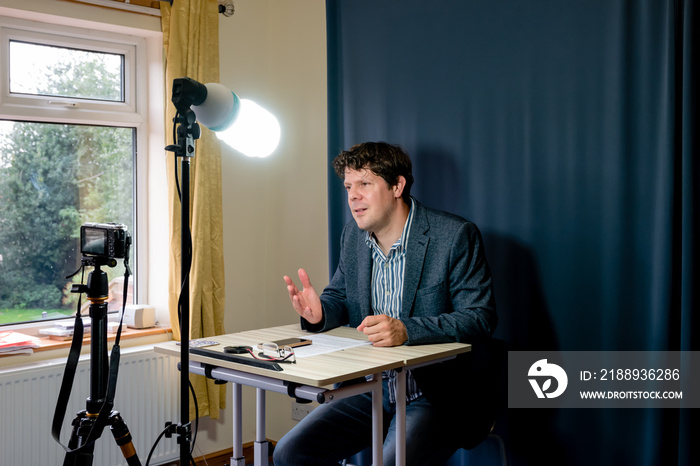 Businessman in makeshift home recording set-up for making videos and calls for remote working