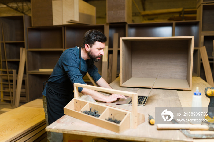 Male carpenter sitting and using a laptop in his workshop